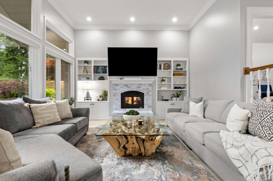 Bright and spacious living room with soaring ceilings, oversized windows, custom built-ins, and a white brick fireplace, featuring modern neutral furnishings and abundant natural light in this updated Canterwood luxury home.